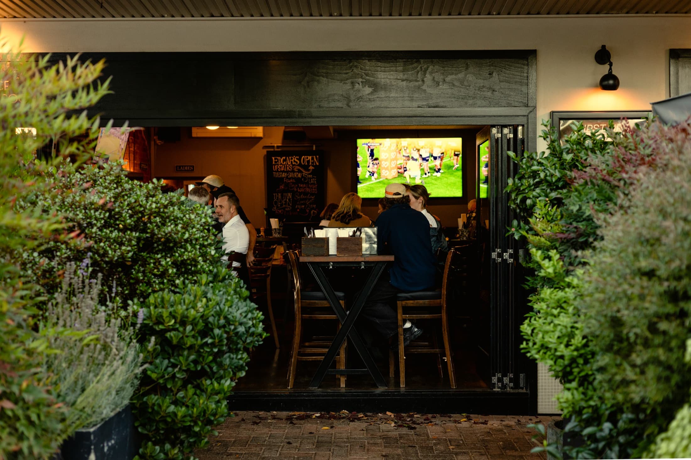 Looking through the beer-garden greenery into Edgar's bar: locals at high tables, footy on the big screen, the specials chalkboard behind